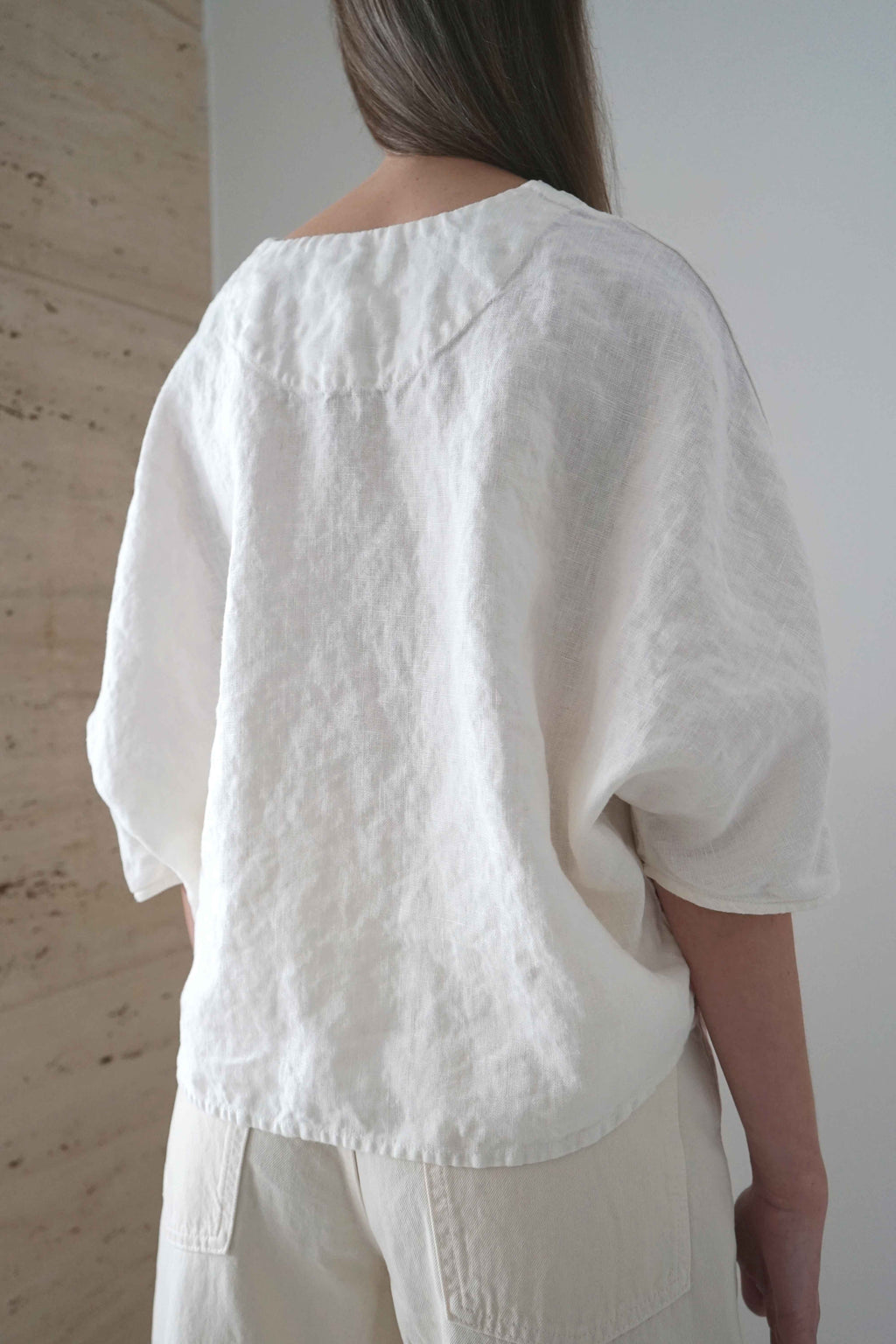 Marei blouse in white, three-quarter back view showing the asymmetric hem