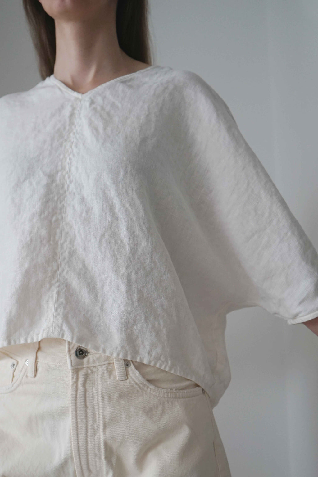 Detail of the three-quarter sleeve and asymmetric hem of the Marei blouse in white