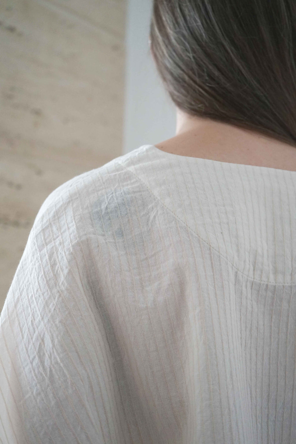 Detail of the back neckline and fine striped fabric of the Marei blouse in beige