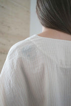 Detail of the back neckline and fine striped fabric of the Marei blouse in beige