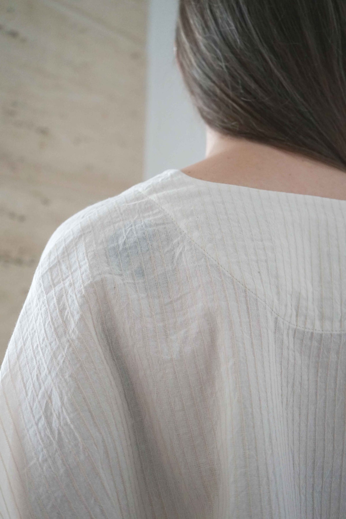 Detail of the back neckline and fine striped fabric of the Marei blouse in beige