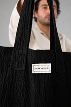 Detalle del tejido negro con textura, las asas y la etiqueta del bolso Leiro