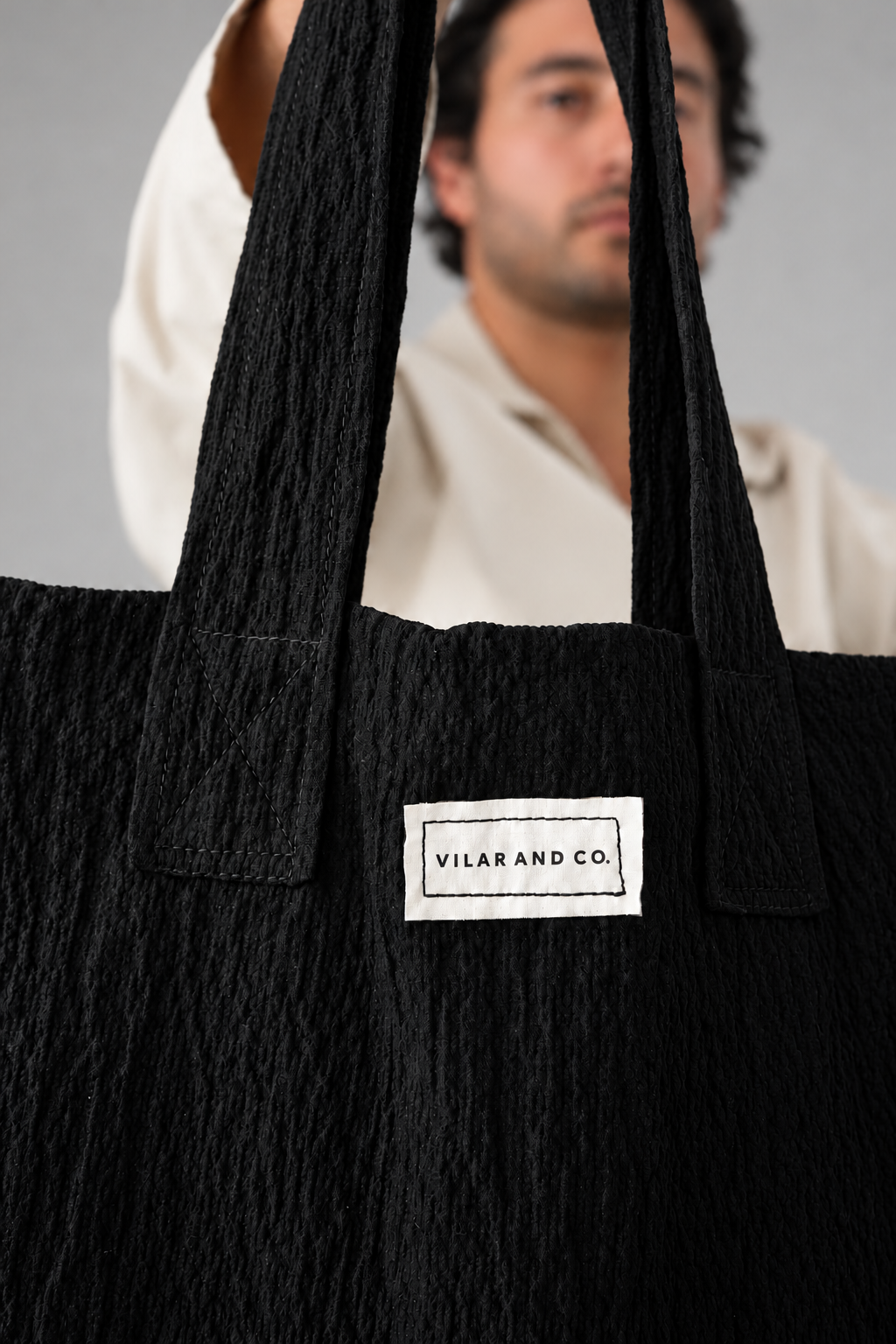 Detalle del tejido negro con textura, las asas y la etiqueta del bolso Leiro